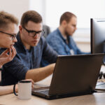 Full concentration at work. Group of young business people working and communicating while sitting at the office desk together with colleagues sitting in the background